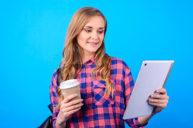 Feche o retrato de um atraente confiante alegre animado inteligente inteligente feliz empresária freelancer aproveitando a loja de chá, assistindo ao vídeo no bloco de pda na mão, isolado na superfície azul