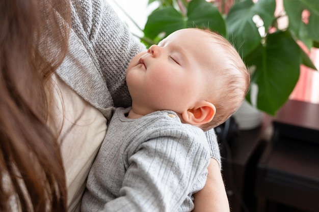 Feche o retrato de um bebê dormindo nos braços da mãe em casa conceito de maternidade feliz