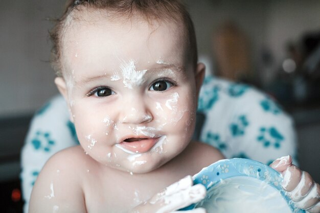 Feche o retrato de um bebê fofo bagunçado que come a sobremesa doce pela primeira vez.