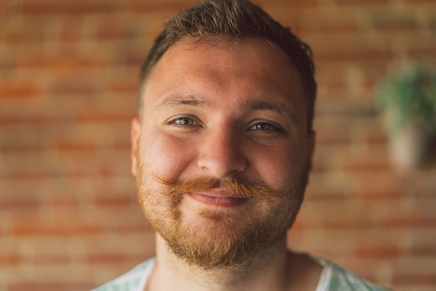 Feche o retrato de um cara bonito e viril com barba e bigode olhando para a câmera e sorrindo alegremente