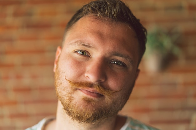 Feche o retrato de um cara bonito e viril com barba e bigode olhando para a câmera e sorrindo alegremente