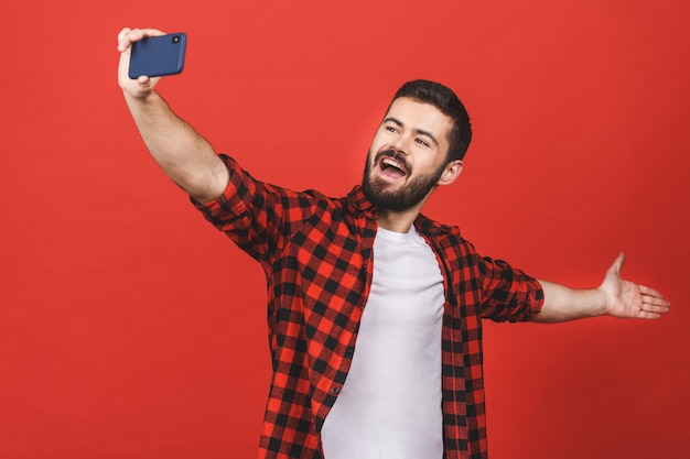 Feche o retrato de um homem barbudo alegre assumindo selfie parede vermelha.