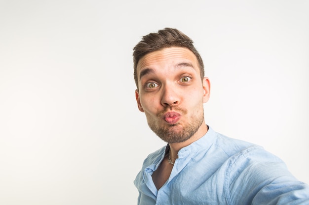 Feche o retrato de um homem barbudo alegre tirando uma selfie sobre uma superfície branca