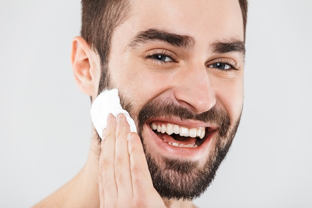 Feche o retrato de um homem barbudo bonito isolado sobre o branco, aplicando espuma de barbear