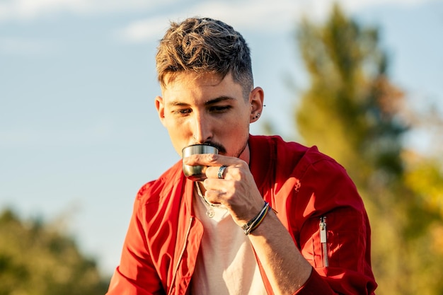 Feche o retrato de um homem bebendo chá na taça da garrafa térmica em um parque durante o pôr do sol