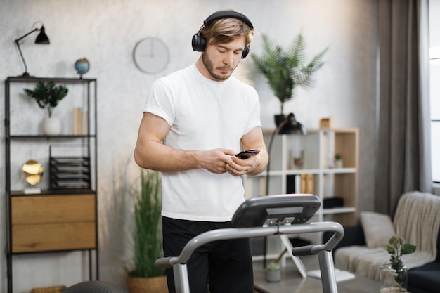 Feche o retrato de um homem musculoso bonito em camiseta branca fazendo exercícios em sua esteira elétrica