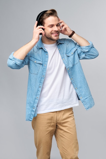 Feche o retrato de um jovem alegre curtindo música, usando uma roupa casual de jeans