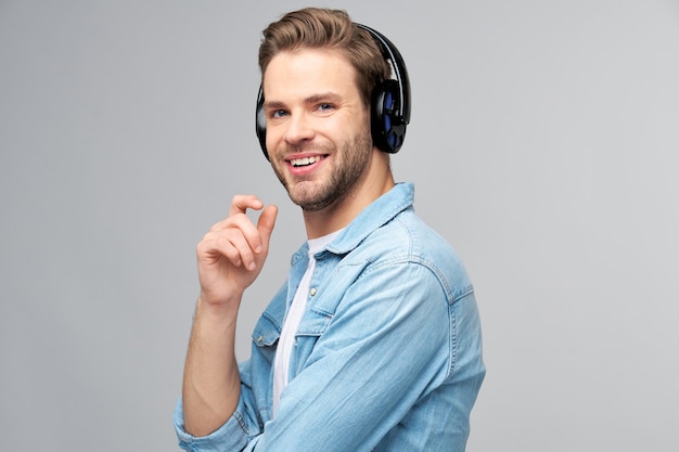 Feche o retrato de um jovem alegre curtindo música, usando uma roupa casual de jeans