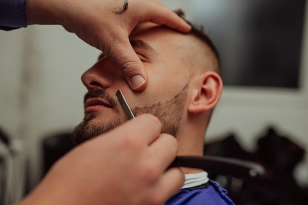 Feche o retrato de um jovem bonito se barbeando com uma navalha Foco na lâmina Foco seletivo Foto de alta qualidade