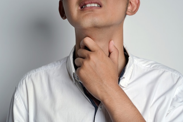 Foto feche o retrato de um jovem com dor de garganta e tocando seu pescoço com as mãos