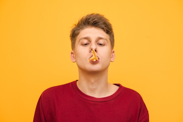 Feche o retrato de um jovem engraçado com batatas fritas na boca.