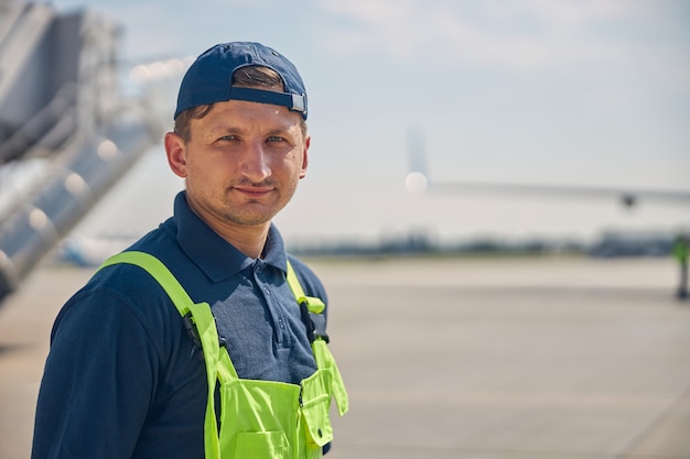 Feche o retrato de um jovem trabalhador do aeroporto com um boné, olhando para a frente