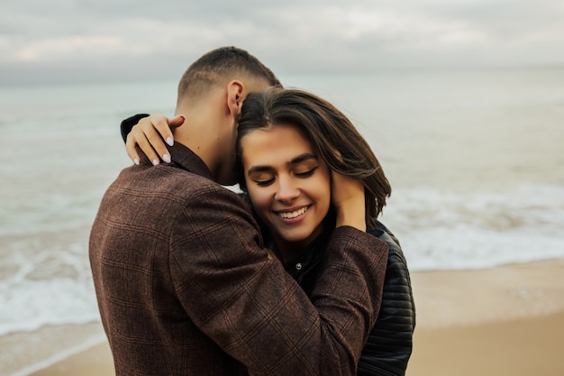 Feche o retrato de um lindo casal apaixonado, abraçando-se enquanto caminhava na praia no mar azul.