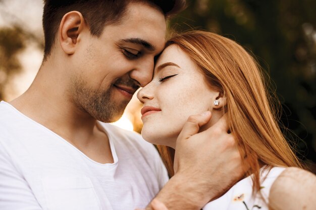 Feche o retrato de um lindo casal jovem se abraçando antes de beijar e sorrir contra o pôr do sol enquanto namorava em seu tempo de férias.