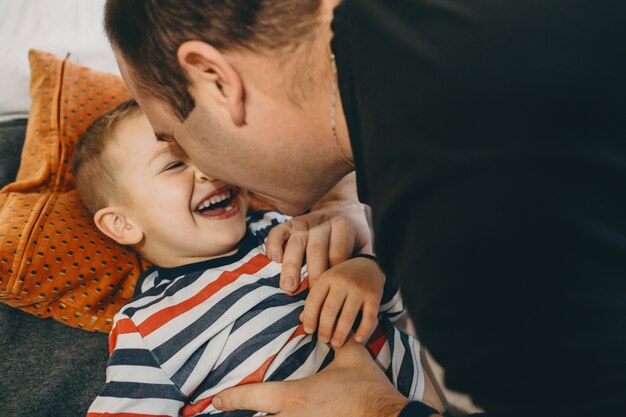 Feche o retrato de um lindo filho brincando com seu pai pela manhã na cama em sua casa.