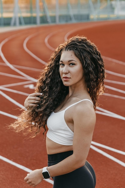 Feche o retrato de um treinador de mulher com cabelo permanente em uma pista de corrida pela manhã.