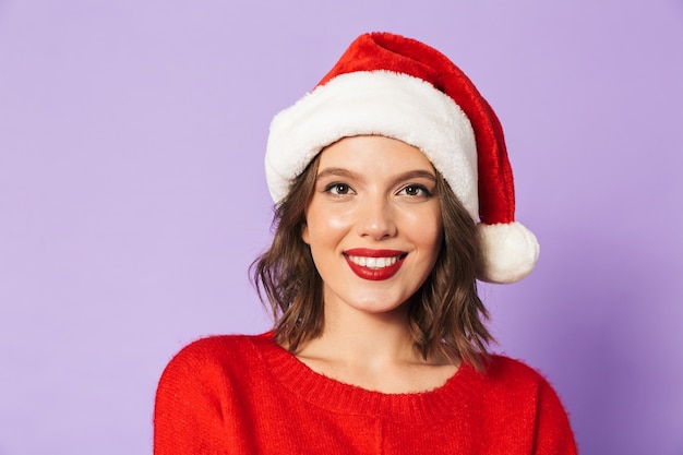 Feche o retrato de uma bela jovem com chapéu de Natal vermelho isolado sobre a parede violeta