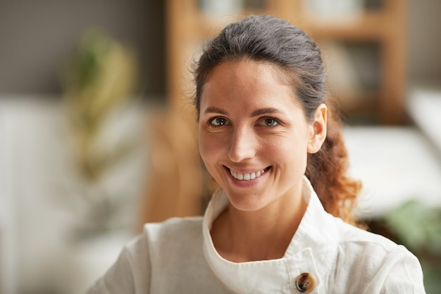 Feche o retrato de uma bela mulher adulta sorrindo para a câmera enquanto vestida com roupas casuais confortáveis em casa ou no escritório, copie o espaço