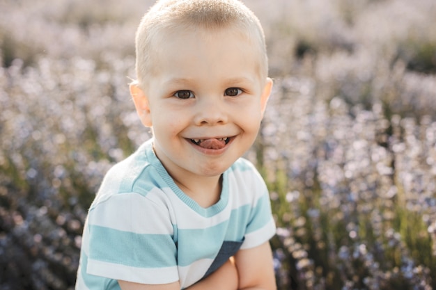 Feche o retrato de uma criança fofa sorrindo mostrar a língua contra um campo de flores.