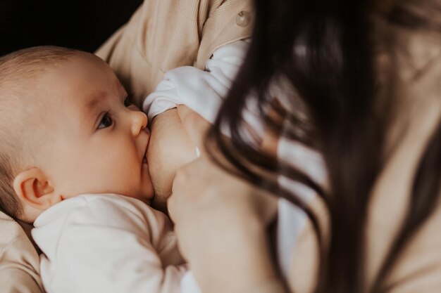 Foto feche o retrato de uma criança que suga o leite do peito da mãe fêmea amamentando sua filhinha em seus braços