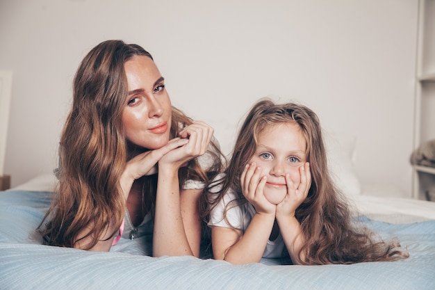 Feche o retrato de uma família amorosa feliz deitada relaxando desfrutando no quarto juntos. mãe e sua filha criança pré-escolar linda garota de pijama deitada na cama.