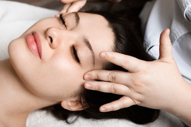 Feche o retrato de uma incrível jovem sentada em um salão de beleza spa, fazendo uma massagem facial antes de fazer a máscara facial.