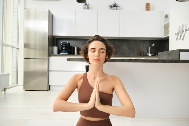 Feche o retrato de uma jovem em casa sentada e meditando praticando ioga fazendo pose de lótus