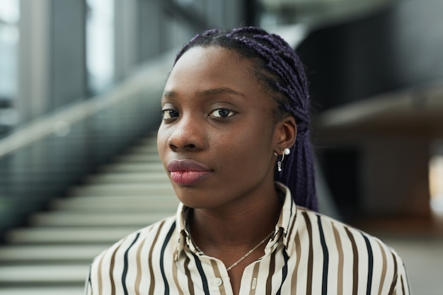 Feche o retrato de uma jovem empresária afro-americana, olhando para a câmera enquanto posa no corredor do escritório, copie o espaço