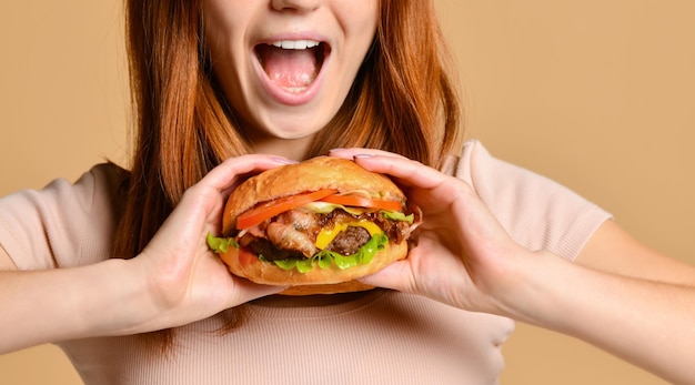 Feche o retrato de uma jovem faminta comendo hambúrguer isolado sobre fundo nu