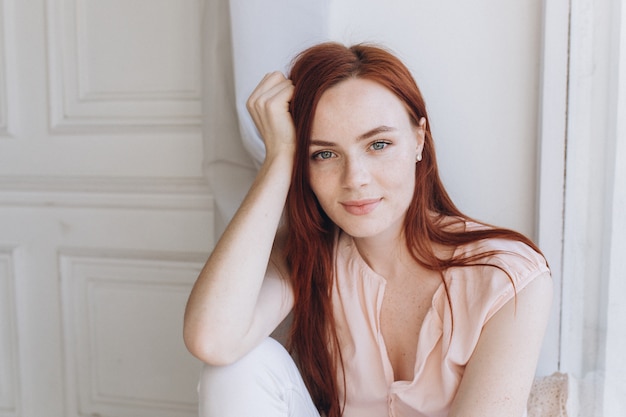 Feche o retrato de uma jovem garota ruiva com rosto sardento dentro de casa