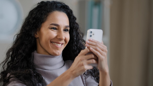 Feche o retrato de uma jovem hispânica feliz segurando o telefone navegando nas redes sociais sorrindo