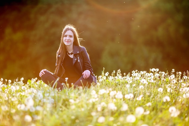 Feche o retrato de uma jovem morena com um colar em volta do pescoço em dentes de leão no pôr do sol