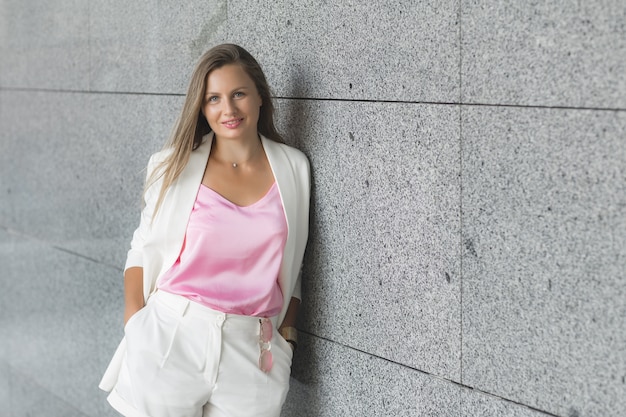 Feche o retrato de uma jovem mulher atraente, vestindo um terno branco ao ar livre. Senhora elegante casaco casual