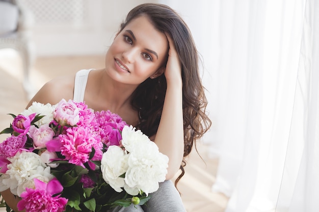 Feche o retrato de uma jovem mulher bonita com flores dentro de casa