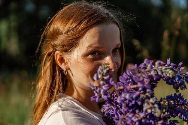 Feche o retrato de uma jovem ruiva linda com sardas usando vestido branco posando na natureza Garota de cabelo vermelho segurando flores Beleza natural Diversidade singularidade individual