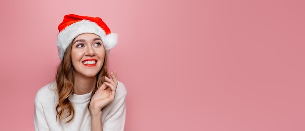 Feche o retrato de uma jovem sorridente feliz com chapéu de Papai Noel isolado em fundo rosa no estúdio