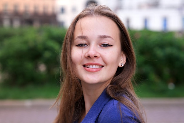 Feche o retrato de uma linda adolescente europeia jovem, feliz e atraente mulher bonita em um dia ensolarado de verão, olhando para a câmera e sorrindo ao ar livre