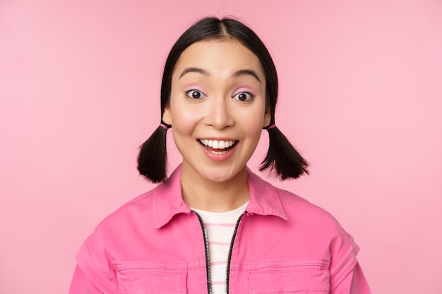 Feche o retrato de uma linda garota asiática parecendo entusiasmada e sorrindo rindo e sorrindo de pé feliz contra o fundo rosa