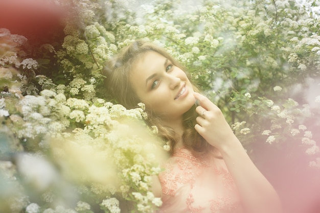 Feche o retrato de uma linda garota em um vestido vintage rosa em pé perto de flores coloridas. Trabalho de arte de mulher romântica. Modelo de ternura bonita, olhando para a câmera.