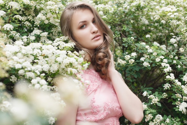 Feche o retrato de uma linda garota em um vestido vintage rosa em pé perto de flores coloridas. Trabalho de arte de mulher romântica. Modelo de ternura bonita, olhando para a câmera.