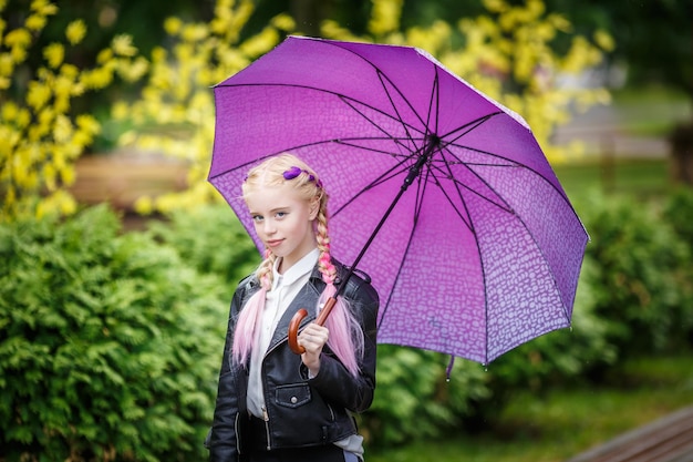 Feche o retrato de uma linda garotinha estilosa com um guarda-chuva na chuva no parque