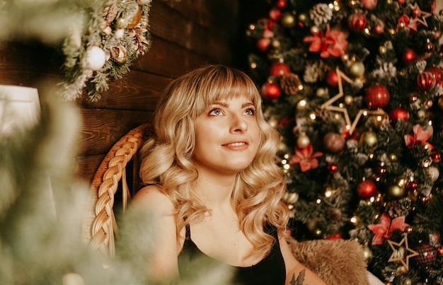 Feche o retrato de uma linda jovem com cabelo longo cacheado em um fundo de Natal com luzes. Foto mágica de ano novo quente. Interior aconchegante.