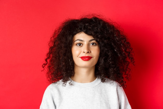 Feche o retrato de uma linda mulher moderna com penteado encaracolado e lábios vermelhos, sorrindo feliz no camer.