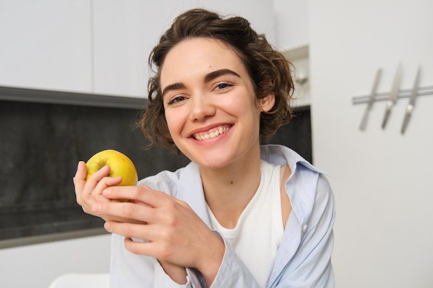 Feche o retrato de uma linda mulher sorridente comendo uma maçã e parecendo feliz para a câmera sentada