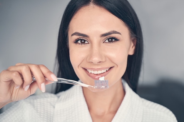 Foto feche o retrato de uma menina com uma quantidade de pasta de dente do tamanho de uma ervilha na escova sorrindo na frente