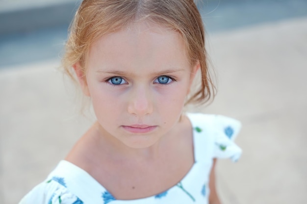Feche o retrato de uma menina pensativa e séria de pré-escola, grandes olhos azuis, olhando para a câmera com um rosto triste e infeliz, tendo problemas para pensar em más relações na família