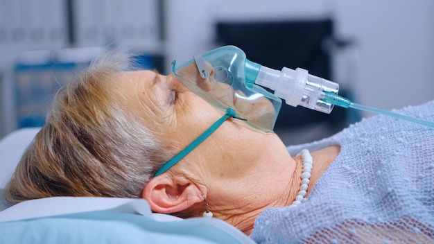 Feche o retrato de uma mulher aposentada respirando com dificuldades na máscara de oxigênio deitada na cama de hospital durante o surto de coronavírus covid-19. sistema de saúde de medicina médica. tratamento de infecção