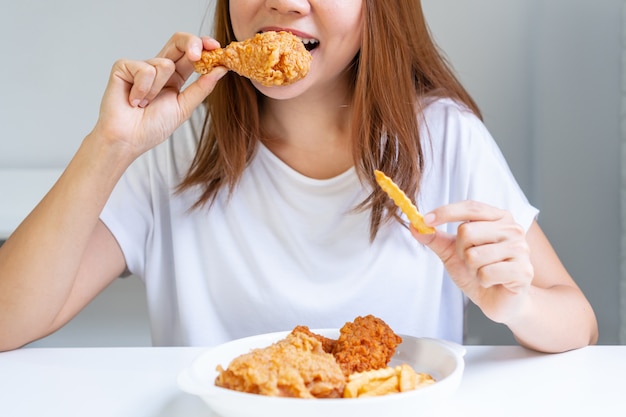 Feche o retrato de uma mulher asiática bonita satisfeita, comendo frango frito e batatas fritas