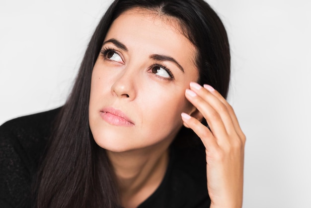 Feche o retrato de uma mulher bonita morena com dor de cabeça tocando seu rosto, olhe para cima Mulher bonita estressada e preocupada em suéter preto sobre fundo cinza claro Cuidados de saúde e medicina