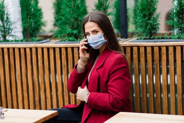 Feche o retrato de uma mulher branca usando uma máscara médica e em pé na rua contra um café